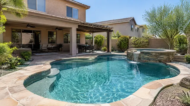 Mid-size backyard of a 2000s two-story Gilbert, Arizona stucco home: free-form pool with a raised spa, aqua finish, flagstone-look coping, a covered patio with ceiling fans and a pergola