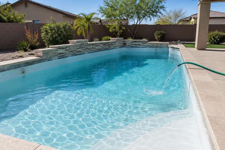 Backyard pool being refilled with a garden hose over a freshly cleaned white plaster floor, water a few feet deep